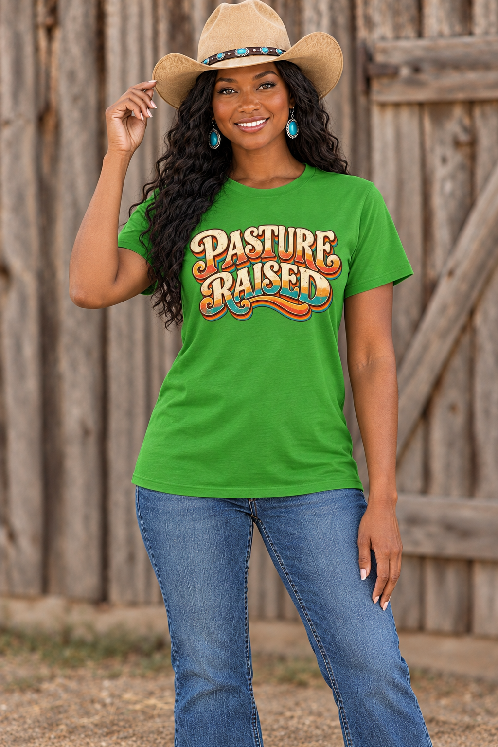 Black cowgirl wearing the green Pasture Raised tee in a new hat-brim pose against rustic barn wood
