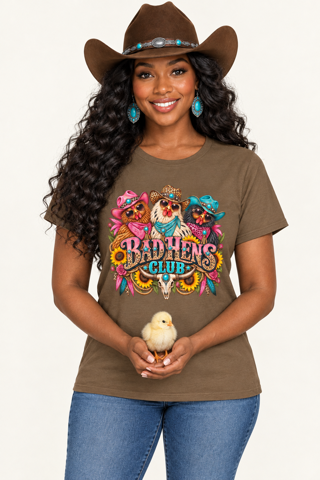 Black cowgirl wearing the saddle-brown Bad Hens Club tee and gently holding a baby chick