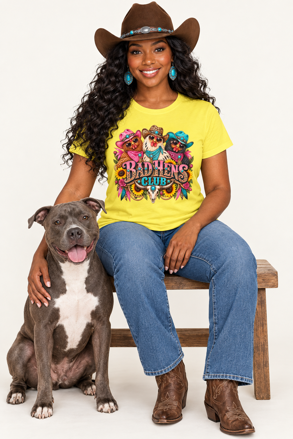 Black cowgirl wearing the yellow Bad Hens Club tee seated beside a pit bull