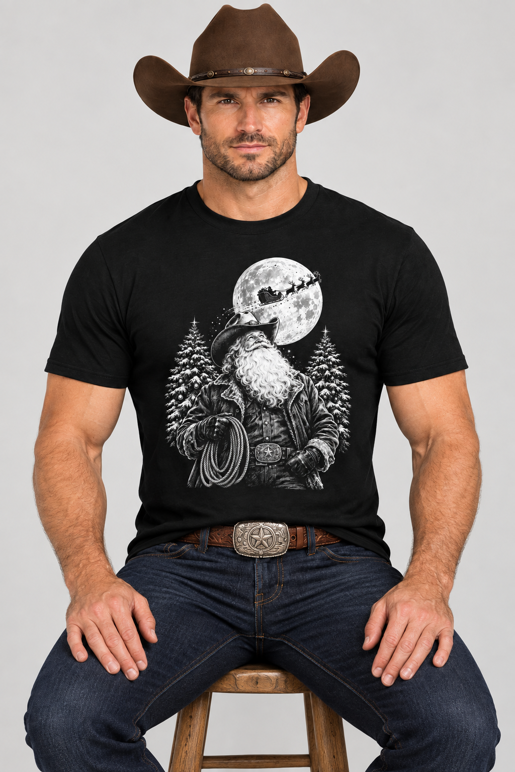Close-up studio mockup of cowboy seated on a stool wearing the black Cowboy Santa tee